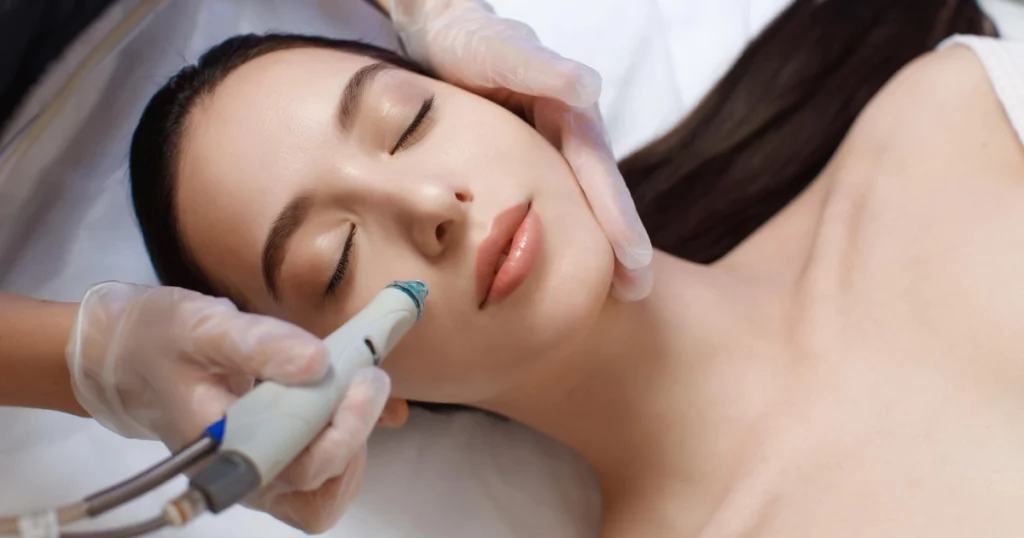 Close-up of a woman receiving a HydraFacial treatment in ERIE, PA as a professional uses a handheld device on her cheek while she relaxes with eyes closed